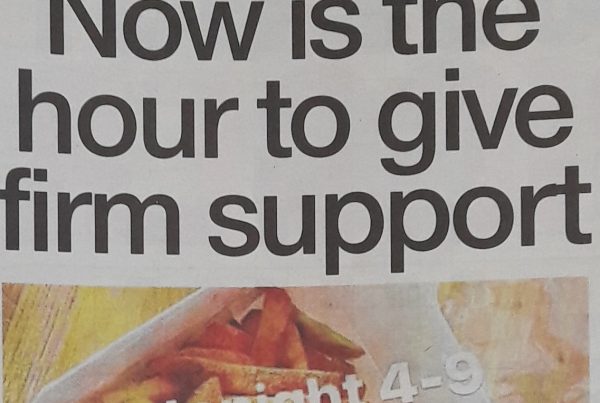 Headline banner featuring “Now is the hour to give firm support” overlaid on an image of local shops with “Support Local” signs in windows, reflecting community resilience during the pandemic.