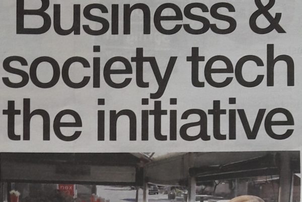 A digital banner featuring the headline “Business and society tech the initiative” with an image showing a person working from home on a laptop, surrounded by digital technology symbols like cloud, app, and connectivity icons.