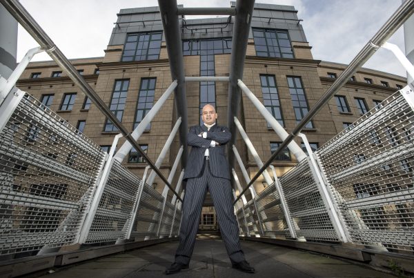 Shaf Rasul standing with arms crossed in front of Edinburgh’s financial district