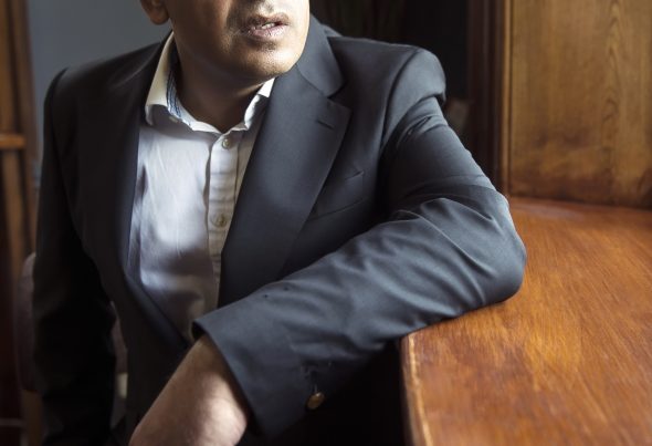 Shaf Rasul wearing a black suit and white shirt, portrait on Shaf Rasul’s website.