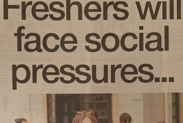 A student in a university dorm with a laptop, socially distanced floor stickers, and a welcome pack, symbolising a pandemic-era freshers' week.