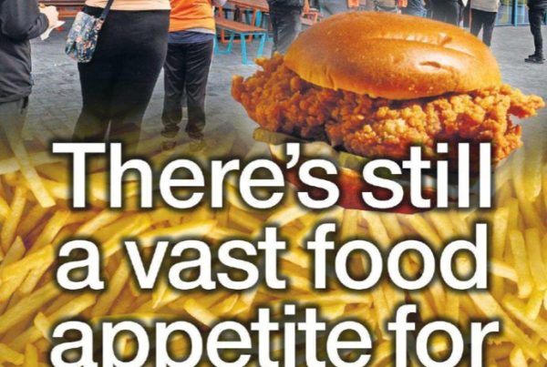 A fast-food counter scene with popular franchise logos like Popeyes, Jollibee, and Five Guys appearing in the background. Customers queue with anticipation, and a bold headline overlay reads: “There’s Still a Vast Food Appetite for Fave Chains”.