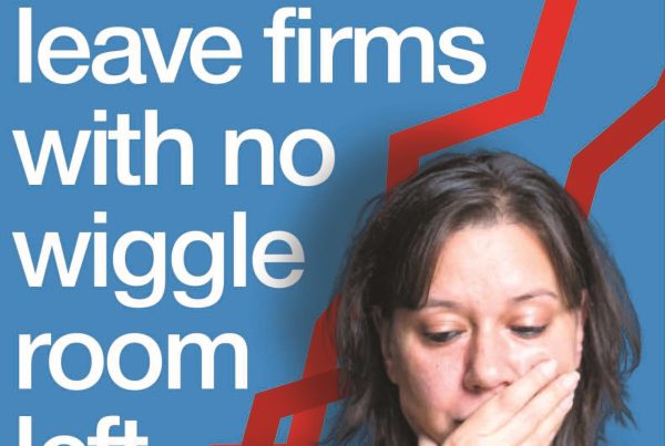 A distressed small business owner checking finances on a laptop in a modest office setting. Headline text reads: “This Financial Crisis Could Leave Firms With No Wiggle Room Left”.