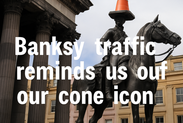 The Duke of Wellington statue in Glasgow, wearing its iconic orange traffic cone atop the rider’s head, with neoclassical columns of the Gallery of Modern Art and surrounding city buildings in the background. The headline “Banksy traffic reminds us of our cone icon” is superimposed in bold white text.